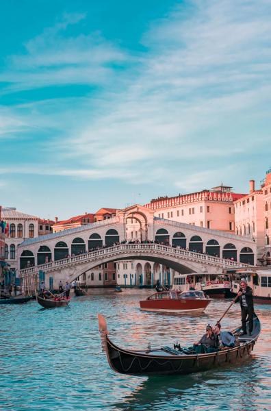 Romantic scene of a gondola in Venice at sunset, with Rialto Bridge in background