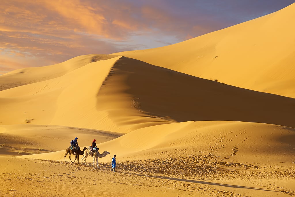 Couple riding camels in Erg Chebbi, Morocco Couple riding camels in Erg Chebbi, Morocco