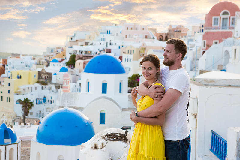 A couple enjoy the view amongst the white and pastel buildings, with famous blue domes in Santorini, Greece