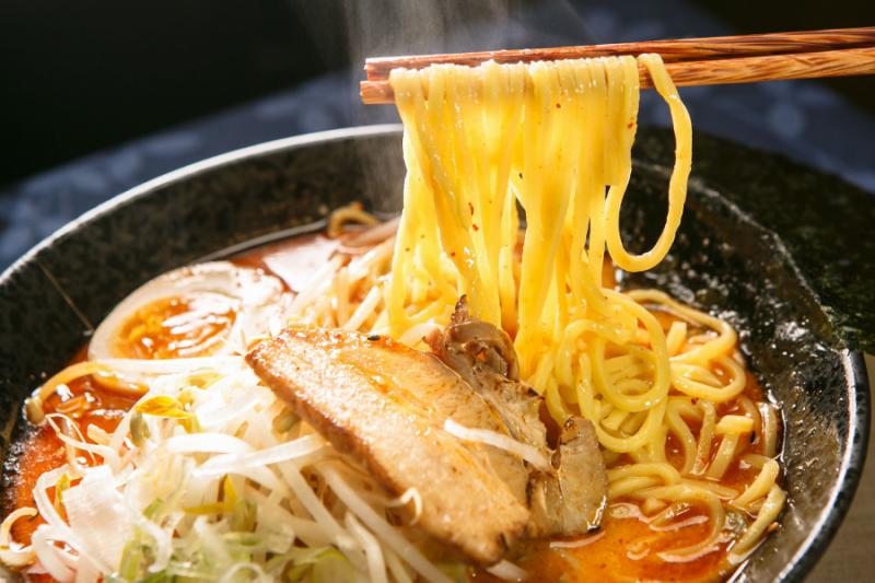 A bowl of miso ramen made with broth that has been seasoned with miso. Japan Tour - Chopsticks Scooping Noodles from Bowl of Miso Ramen